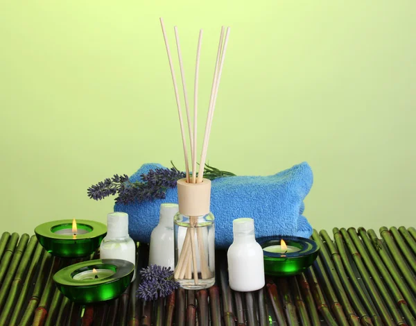 Ambientador de ar, garrafas, toalha e velas no tapete de bambu no fundo verde — Fotografia de Stock