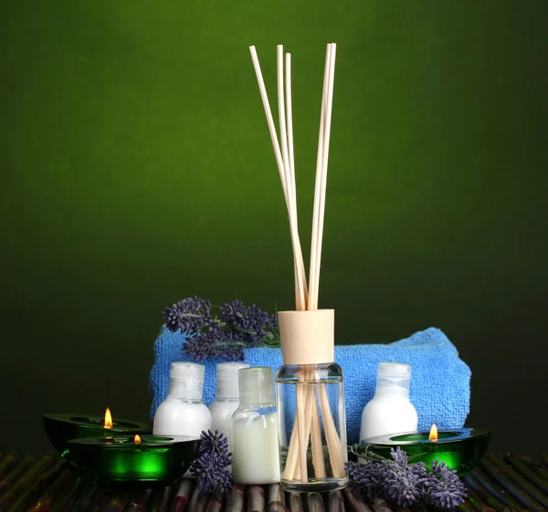 Luftfräschare, flaskor, handduk och ljus på bambu matta på grön bakgrund — Stockfoto