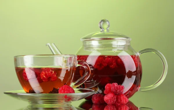 Černé ovoce, malinový čaj v skleněné konvice a šálek na zeleném pozadí — Stock fotografie