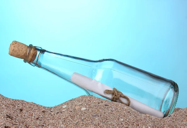 Glass bottle with note inside on sand on blue background — Stockfoto