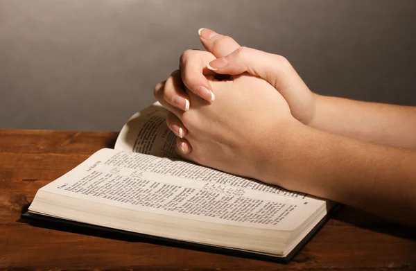 Hände im Gebet über offener russischer Heiliger Bibel auf schwarzem Hintergrund gefaltet — Stockfoto