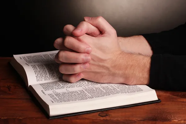 Τα χέρια διπλωμένα στην προσευχή πάνω από μια Αγία Γραφή στο ξύλινο τραπέζι σε γκρι φόντο — Φωτογραφία Αρχείου