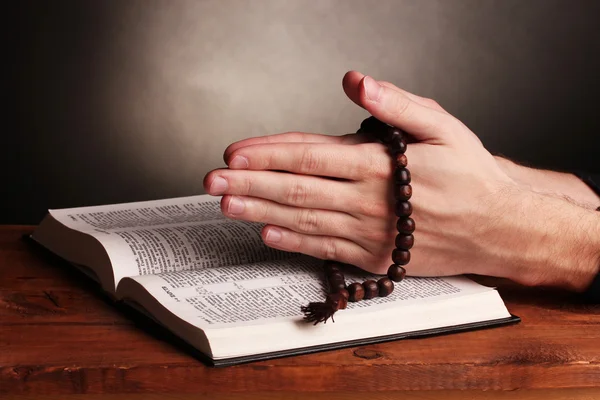 Hands holding wooden rosary over open russian holy bible on grey background — Stock Photo, Image