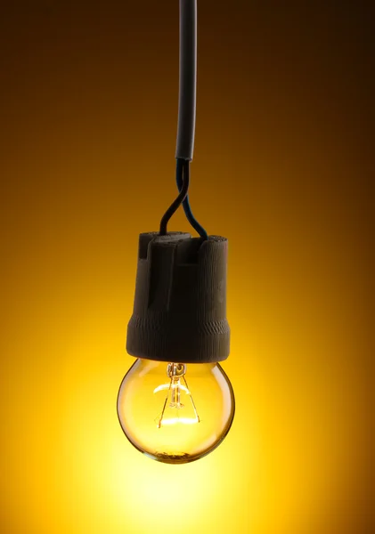 A lit light bulb on yellow background — Stock Photo, Image