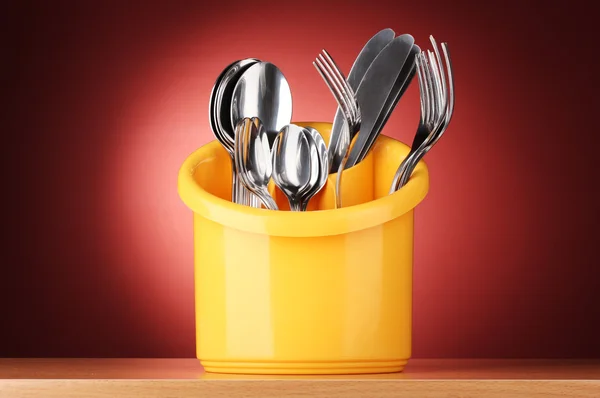 Posate da cucina, coltelli, forchette e cucchiai in stativo giallo su fondo rosso — Foto Stock