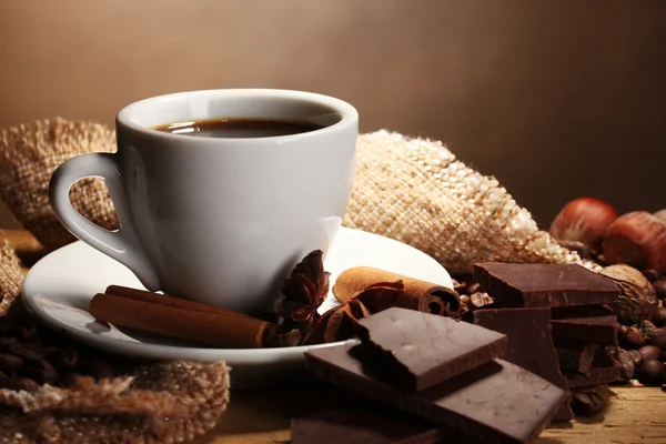 Tasse à café et haricots, bâtonnets de cannelle, noix et chocolat sur table en bois o — Photo