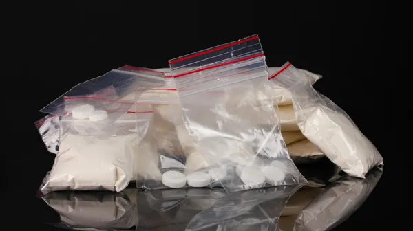 Cocaína e drogas em embalagens em fundo preto — Fotografia de Stock