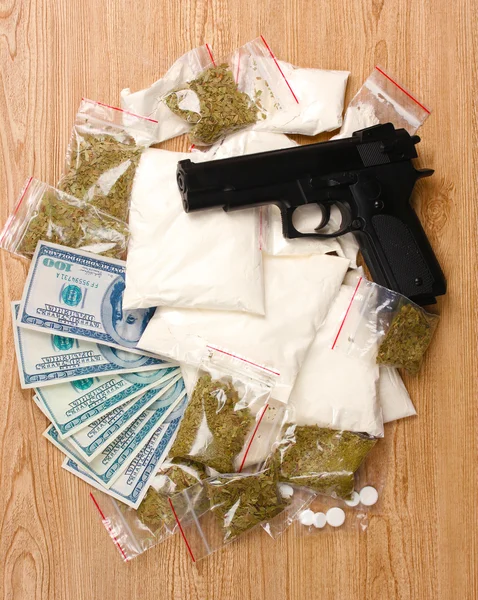 Cocaïne en marihuana in pakketten, dollars en pistool op houten achtergrond — Stockfoto