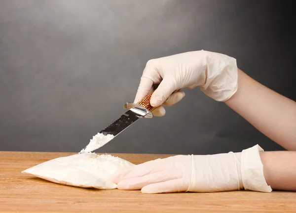 stock image Packets of cocaine opening with a knife on wooden table on grey background