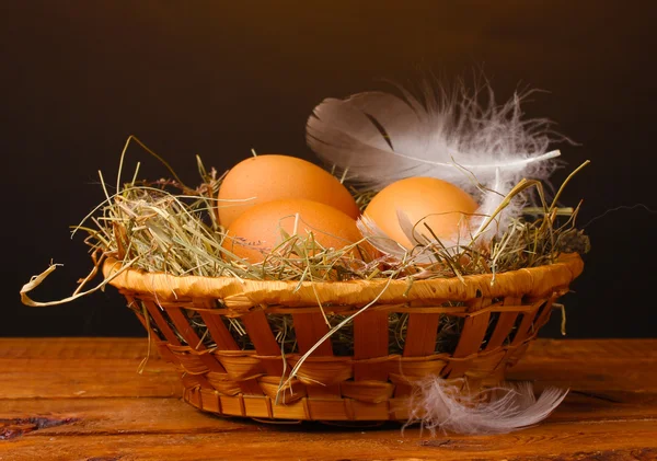 Chicken eggs in a nest on wooden table on brown background — Stock Photo, Image