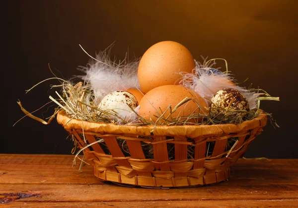 Chicken and quail eggs in a nest on wooden table on brown background — Stock Photo, Image