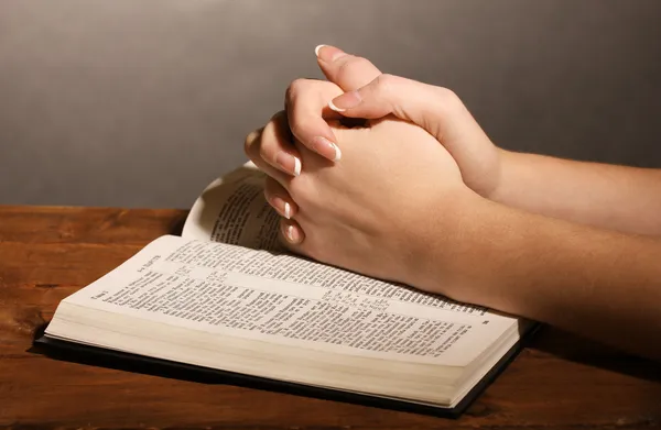 Hands folded in prayer over open russian Holy Bible on black background — Stock Photo, Image