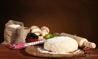 Ingredients for homemade pizza on wooden table on brown background clipart