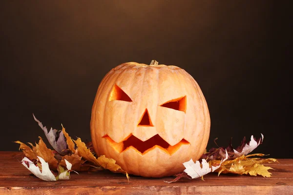 Calabaza de Halloween y hojas de otoño sobre mesa de madera sobre fondo marrón —  Fotos de Stock