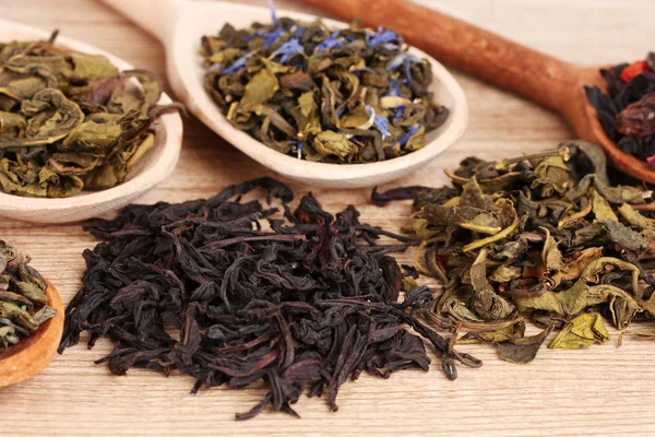 Différents types de thé vert sec et noir dans des cuillères sur fond en bois — Photo