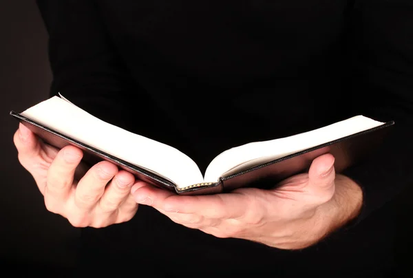 Hände mit offener russischer Bibel auf schwarzem Hintergrund — Stockfoto