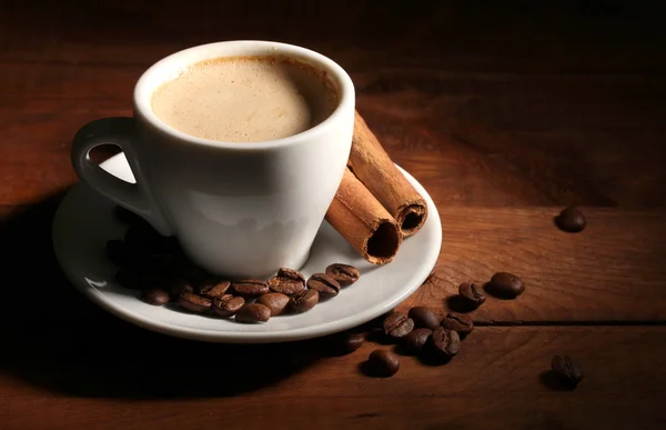 Kopp med kaffe, kanel och kaffe bönor på träbord — Stockfoto