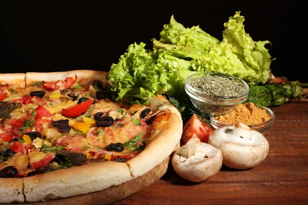 Leckere Pizza, Gemüse und Gewürze auf Holztisch vor braunem Hintergrund — Stockfoto