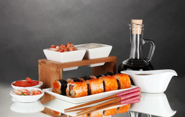 Delicious sushi on plate, chopsticks, soy sauce, fish and shrimps on gray b — Stock Photo, Image