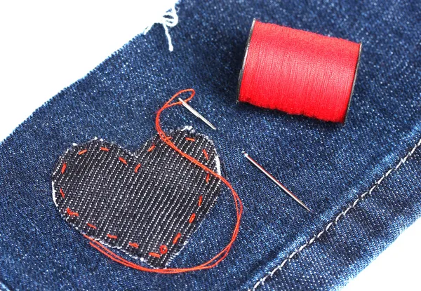 Пластырь в форме сердца на джинсах с иглой и ниткой крупным планом — стоковое фото