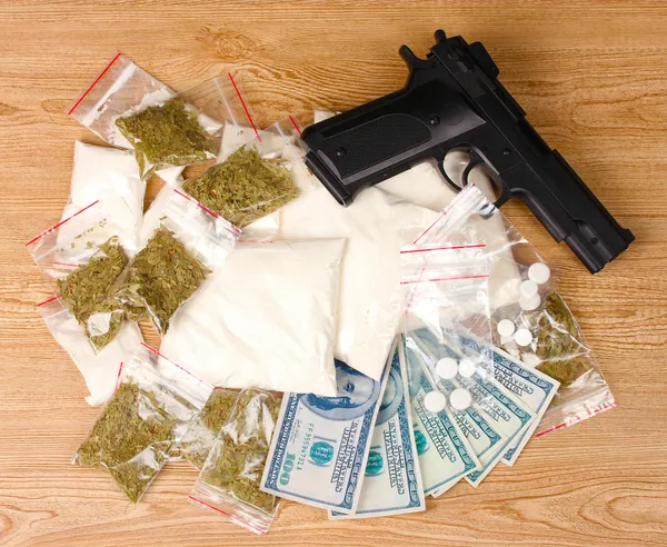 Kokainu a marihuany v obalech, dolary a pistole na dřevěné pozadí — Stock fotografie