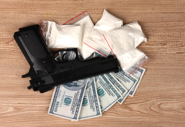Кокаин в упаковках, долларах и пистолетах на деревянном фоне
