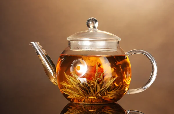 Glas-Teekanne mit exotischem grünen Tee auf Holztisch auf braunem Hintergrund — Stockfoto
