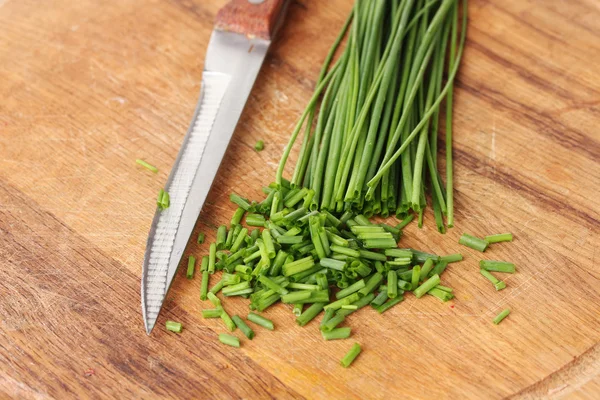 Piękna zielona cebula, szczypiorek i nóż na desce zbliżenie — Zdjęcie stockowe
