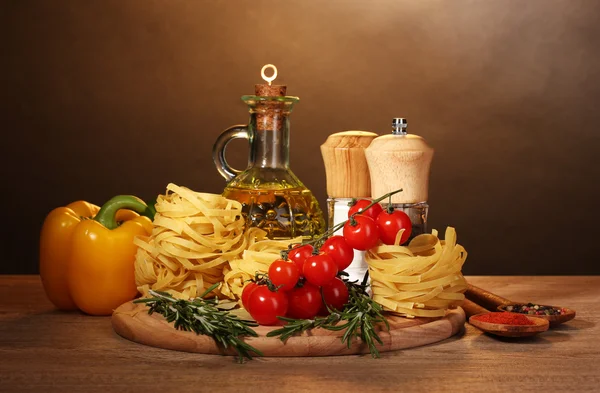 Лапша в миске, банка масла, специи и овощи на деревянном столе на коричневом — стоковое фото