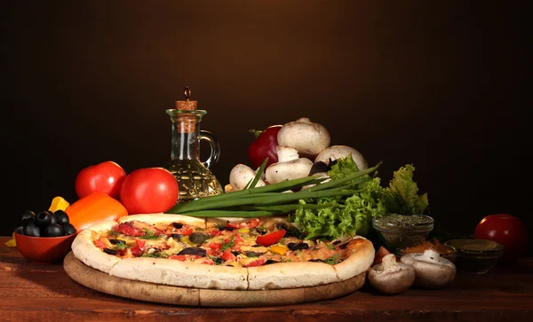 Läcker pizza, grönsaker och kryddor på träbord på brun bakgrund — Stockfoto
