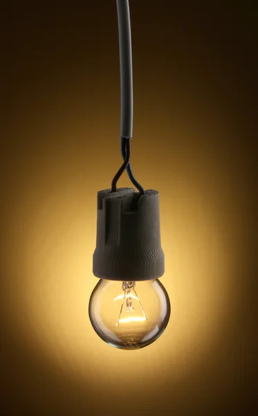 En tänd glödlampa på gul bakgrund — Stockfoto