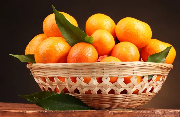 Mandarinen mit Blättern in einem schönen Korb auf einem Holztisch auf braunem Rücken — Stockfoto