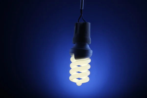 Una bombilla de ahorro de energía iluminada sobre fondo azul — Foto de Stock