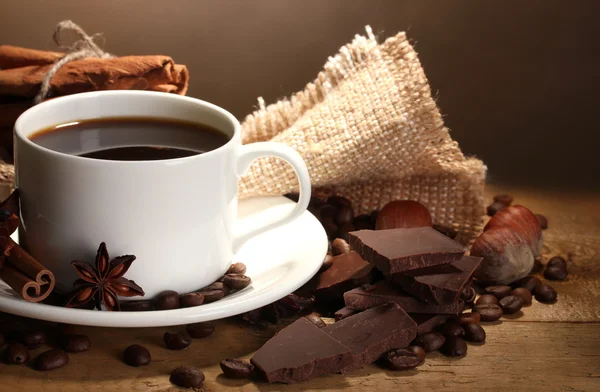 Кофейная чашка и бобы, коричные палочки, орехи и шоколад на деревянном столе — стоковое фото