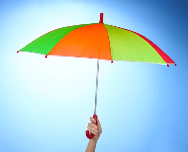 Mehrfarbiger Regenschirm in der Hand auf blauem Hintergrund — Stockfoto