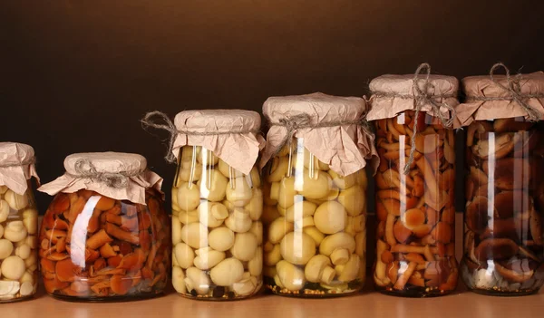 Deliciosos cogumelos marinados nos frascos de vidro na prateleira de madeira — Fotografia de Stock