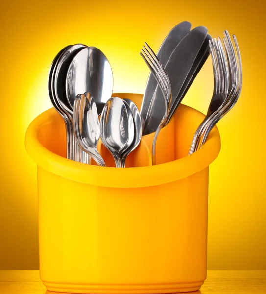 Kitchen cutlery, knives, forks and spoons in yellow stand on yellow backgro — Stock Photo, Image