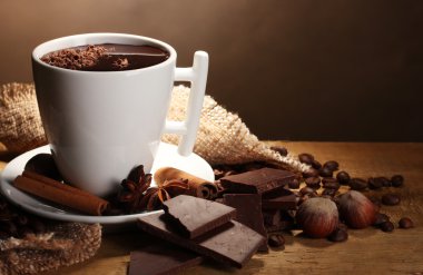 Cup of hot chocolate, cinnamon sticks, nuts and chocolate on wooden table o clipart