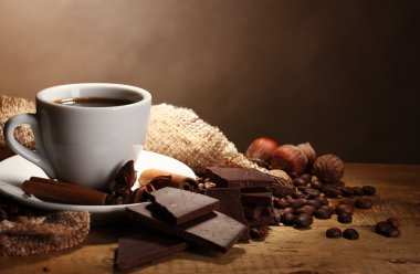 Coffee cup and beans, cinnamon sticks, nuts and chocolate on wooden table o clipart