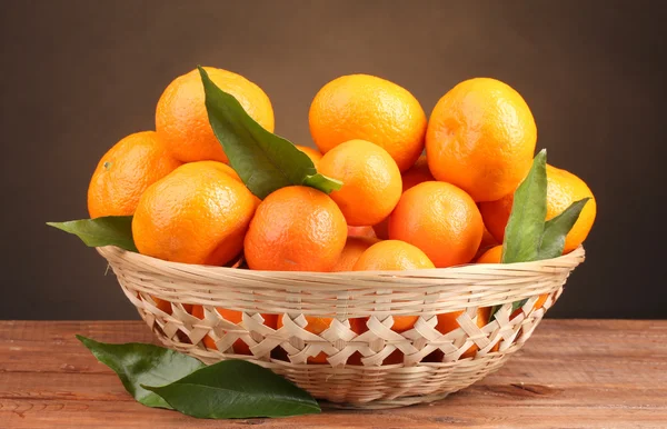 Tangerines with leaves in a beautiful basket on wooden table on brown backg — Stock Photo, Image