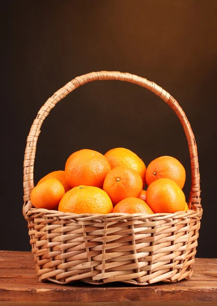 Tangerines in a beautiful basket on wooden table on brown background — Stock Photo, Image