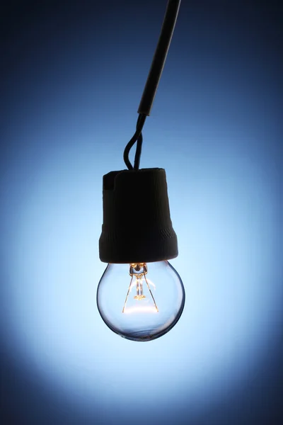A lit light bulb on blue background — Zdjęcie stockowe