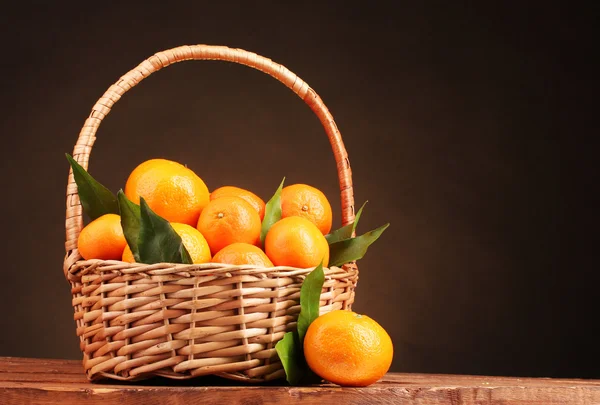 Mandarinas con hojas en una hermosa canasta sobre mesa de madera sobre respaldo marrón — Foto de Stock