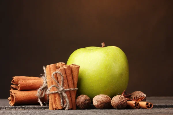 Cinnamon sticks, green apple and nutmeg on wooden table on brown background — Stock Photo, Image