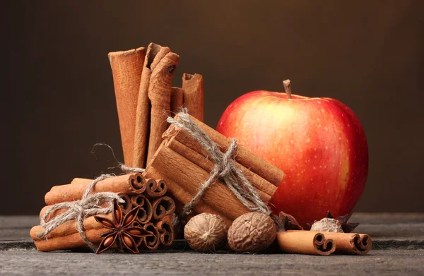 Varas de canela, maçã vermelha, noz-moscada e anis na mesa de madeira no backgr marrom — Fotografia de Stock