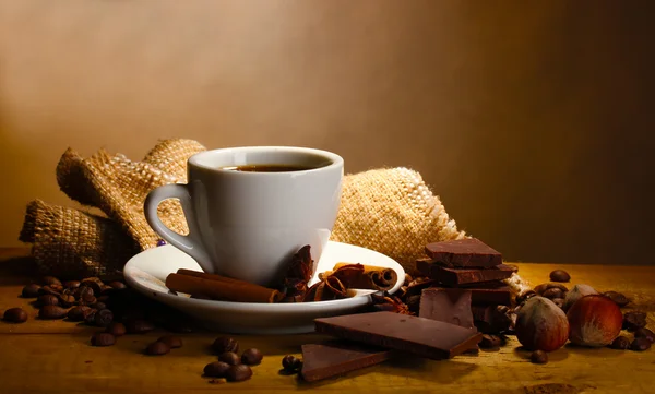 Koffie beker en bonen, kaneelstokjes, noten en chocolade op houten tafel — Stockfoto