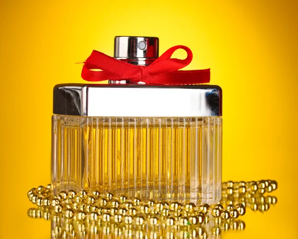Perfume bottle with red bow on yellow background — Stock Photo, Image