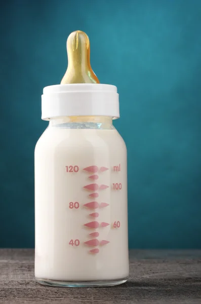 Baby bottle of milk on wooden table on blue background — Stock Photo, Image