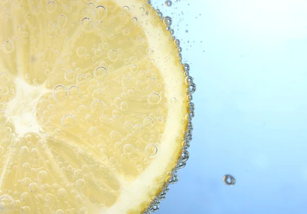 Zitronenscheibe im blauen Wasser mit Blasen — Stockfoto