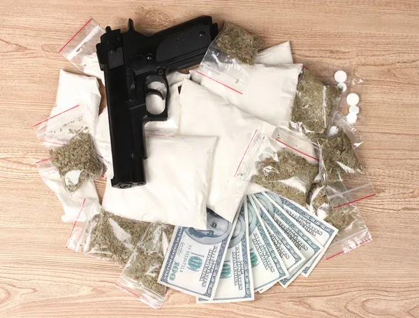 Cocaïne et marihuana en paquets, dollars et arme de poing sur fond en bois — Photo